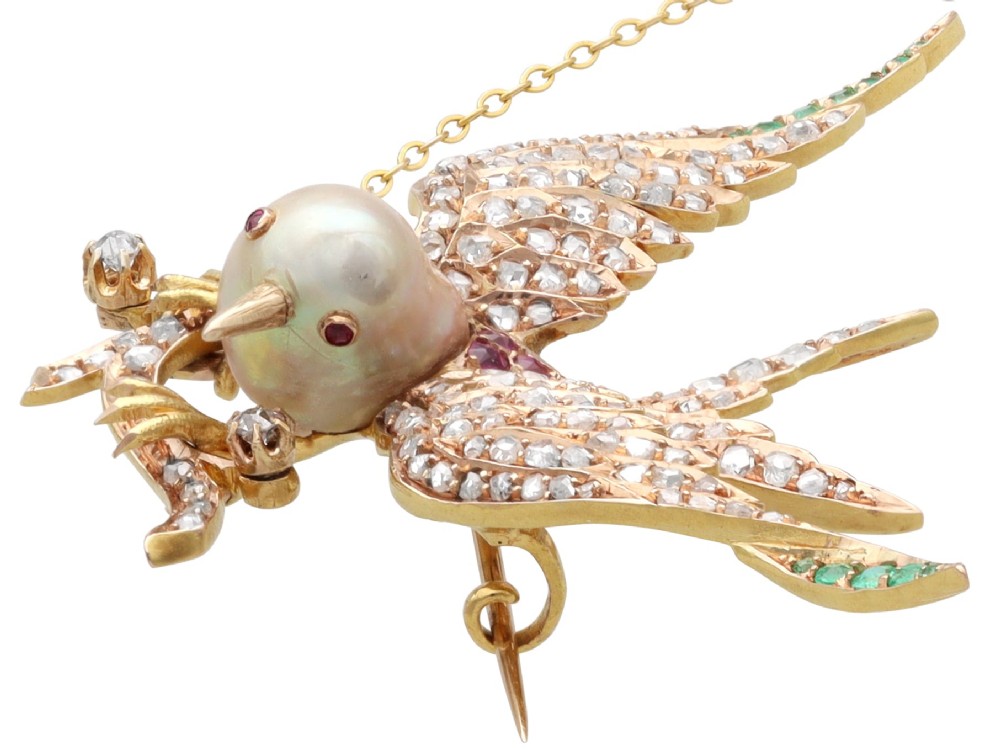 An antique Victorian 18ct yellow gold bird brooch set with diamonds on the wings, emeralds along the outer feathers, a natural pearl body, and ruby details. View VI
