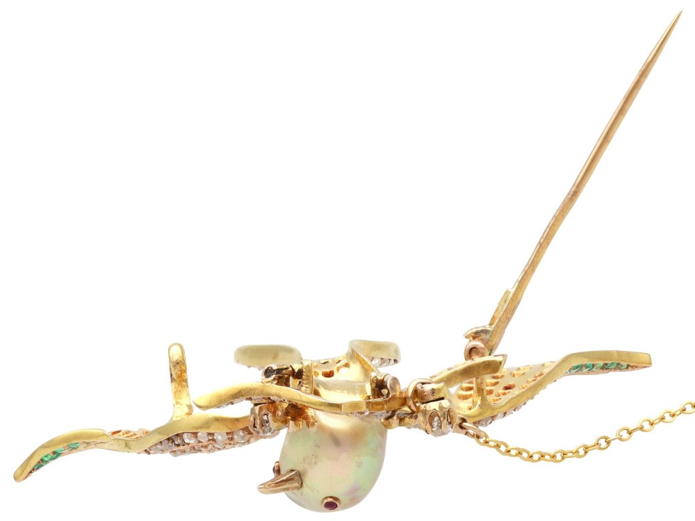 An antique Victorian 18ct yellow gold bird brooch set with diamonds on the wings, emeralds along the outer feathers, a natural pearl body, and ruby details. View IX
