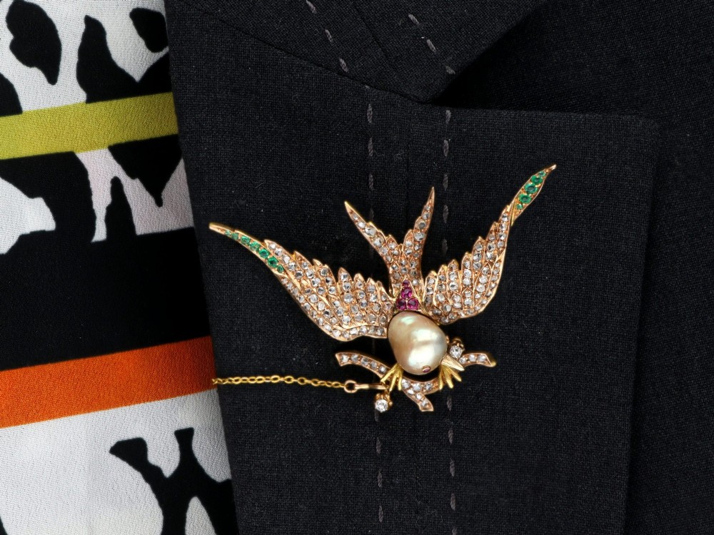 An antique Victorian 18ct yellow gold bird brooch set with diamonds on the wings, emeralds along the outer feathers, a natural pearl body, and ruby details. View XI