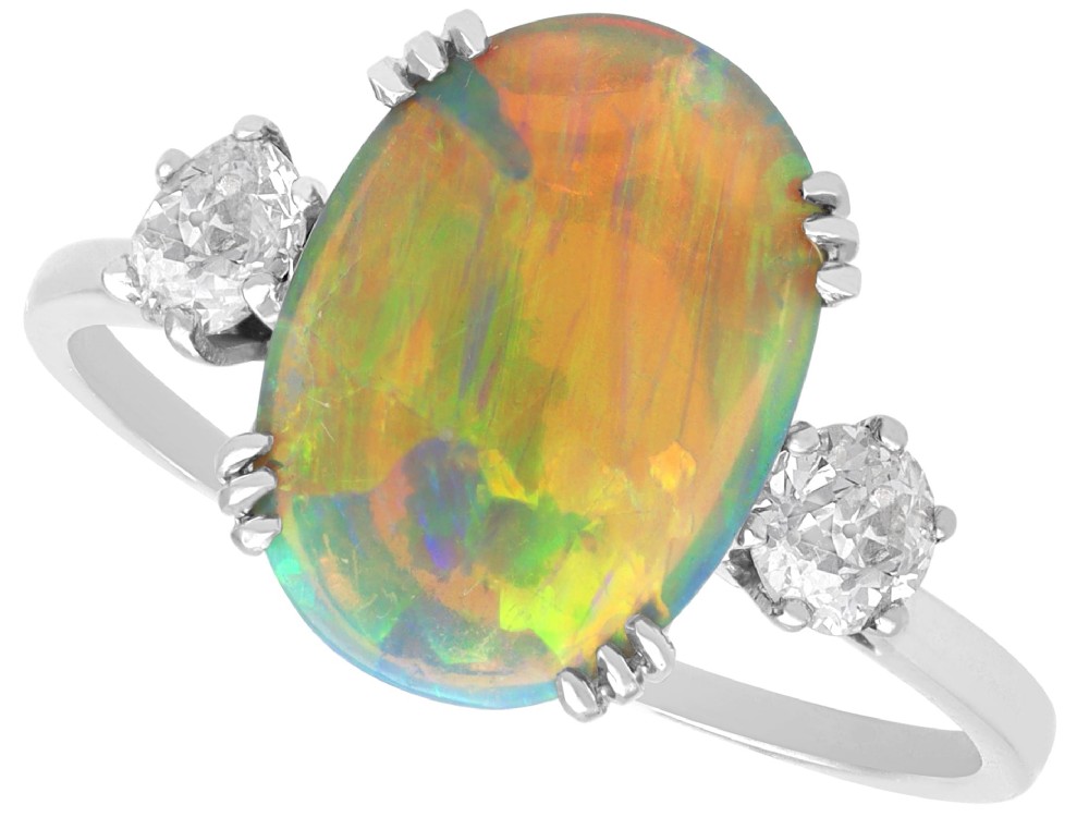An antique platinum trilogy ring featuring a central oval cabochon opal flanked by two round cut diamonds.