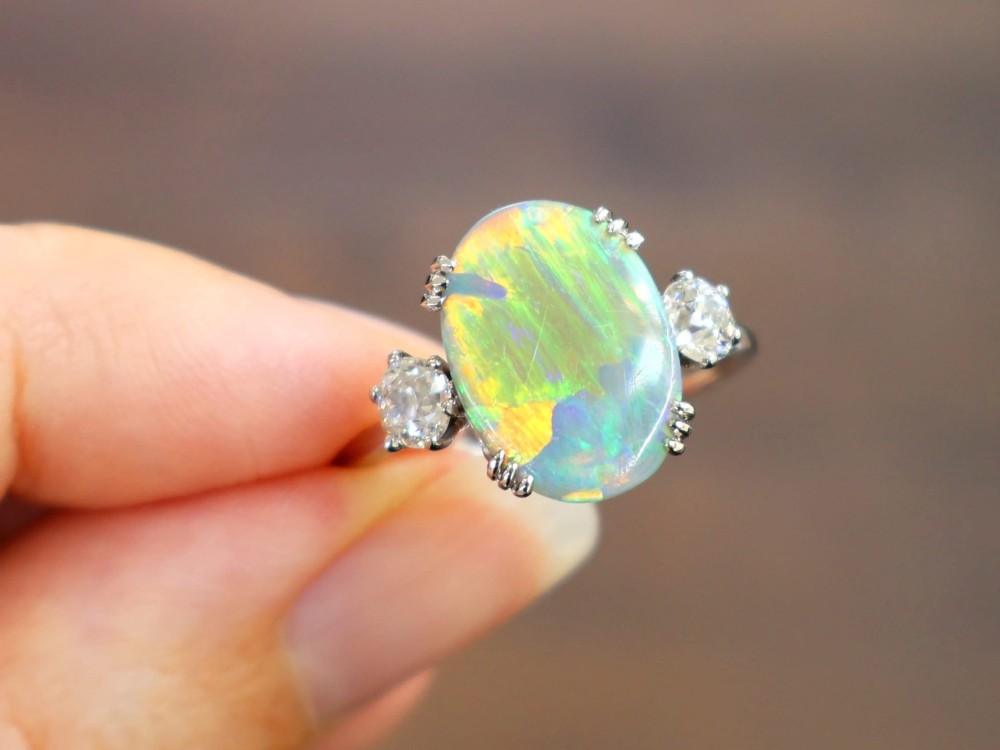 An antique platinum trilogy ring featuring a central oval cabochon opal flanked by two round cut diamonds. View III