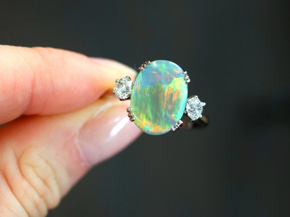 An antique platinum trilogy ring featuring a central oval cabochon opal flanked by two round cut diamonds. View IV
