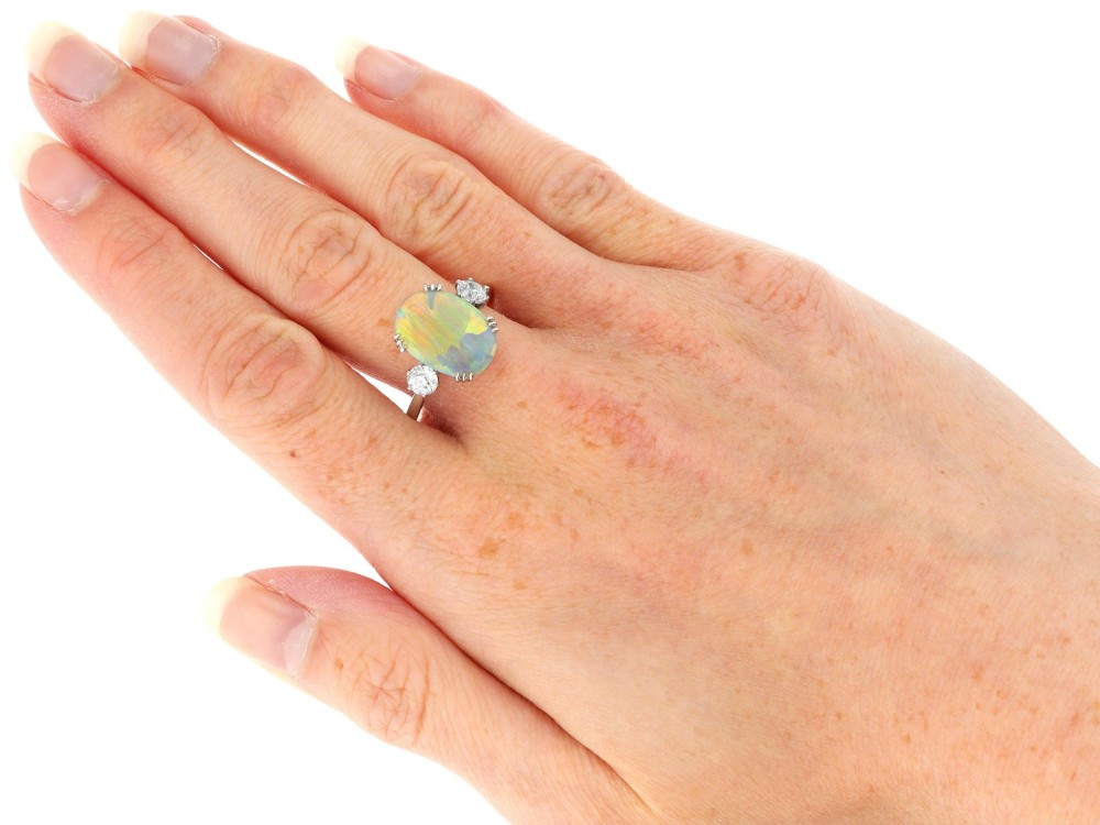 An antique platinum trilogy ring featuring a central oval cabochon opal flanked by two round cut diamonds. View X