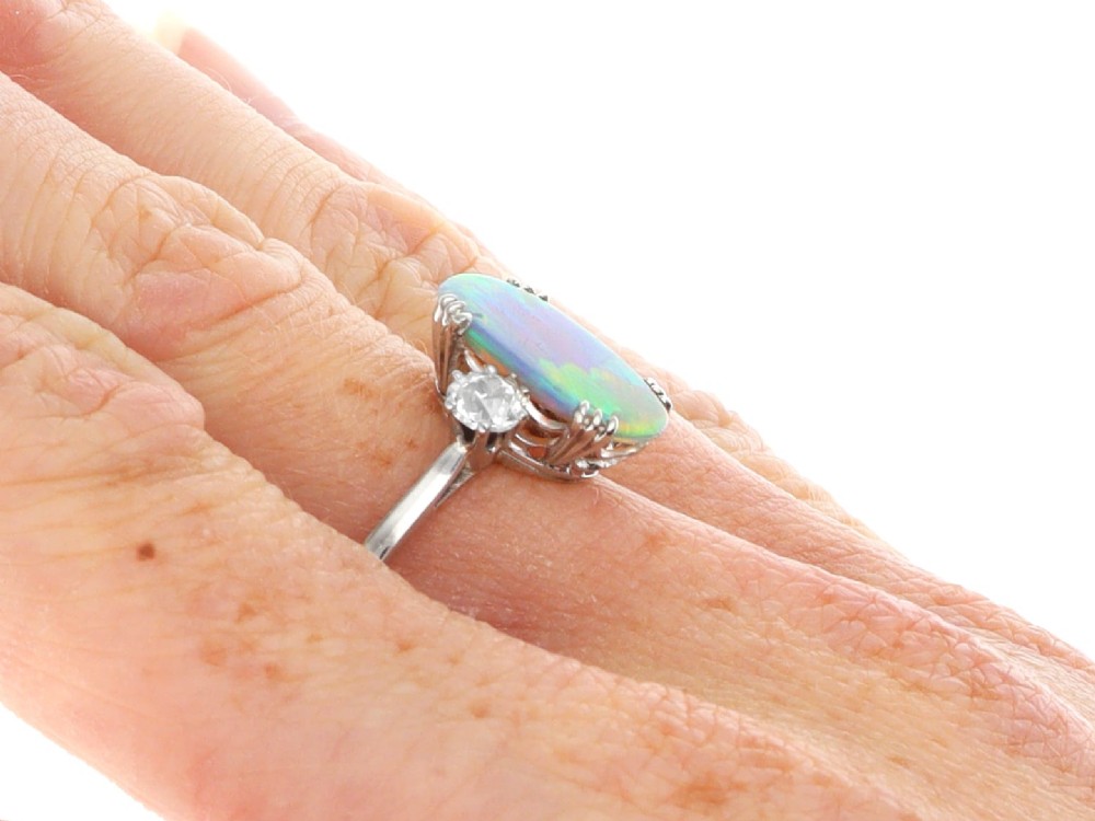 An antique platinum trilogy ring featuring a central oval cabochon opal flanked by two round cut diamonds. View XI