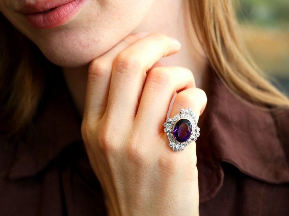 An Art Deco ring featuring a central oval purple amethyst set in yellow gold, framed by a millegrain diamond halo. View IV