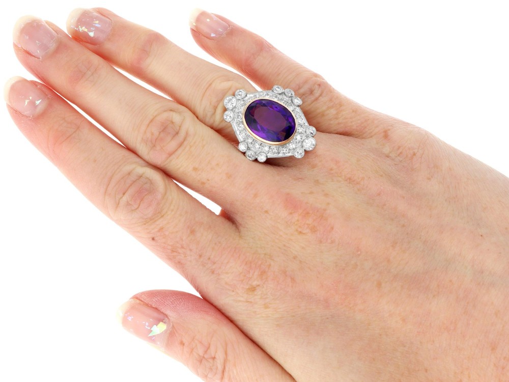An Art Deco ring featuring a central oval purple amethyst set in yellow gold, framed by a millegrain diamond halo. View X