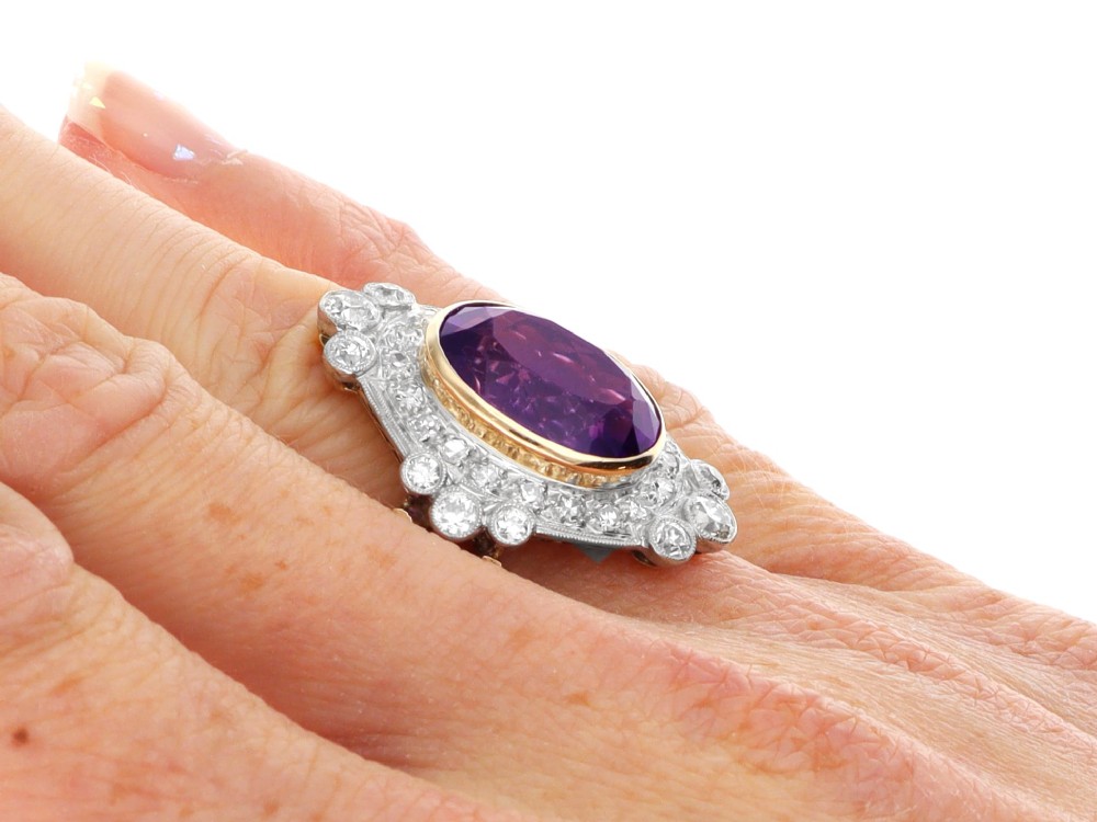 An Art Deco ring featuring a central oval purple amethyst set in yellow gold, framed by a millegrain diamond halo. View XI