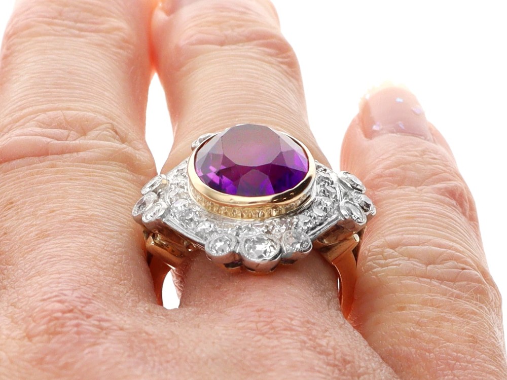 An Art Deco ring featuring a central oval purple amethyst set in yellow gold, framed by a millegrain diamond halo. View XII