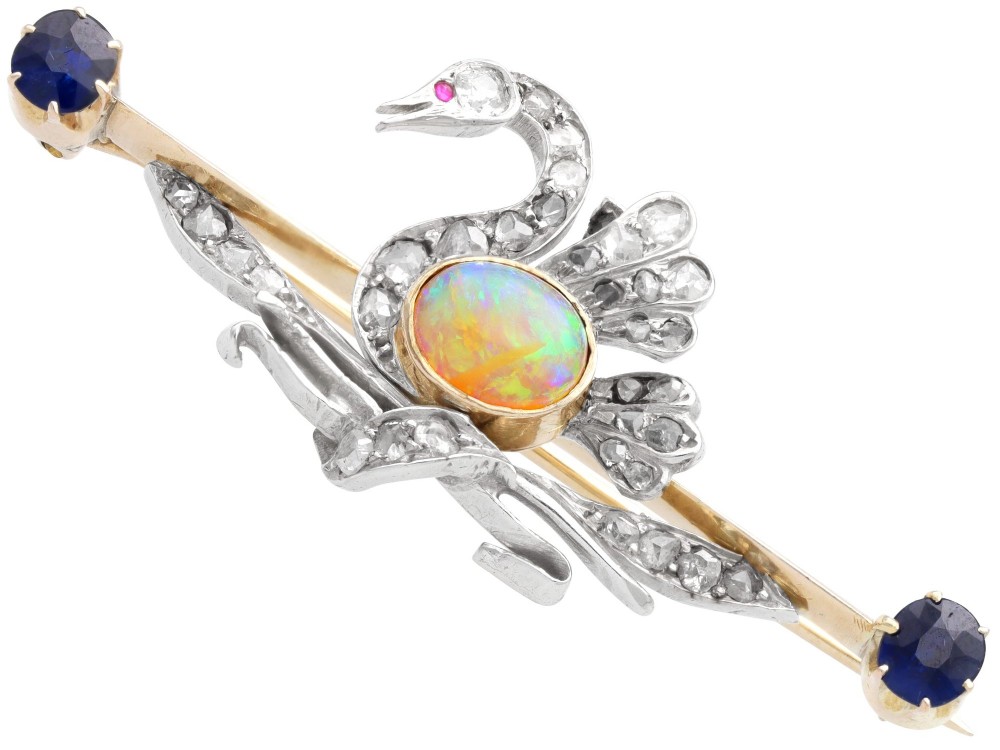 An antique Victorian 9ct gold bar brooch featuring a central swan motif set with diamonds and an oval opal body, flanked by two blue sapphires. View VI
