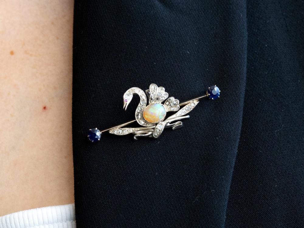 An antique Victorian 9ct gold bar brooch featuring a central swan motif set with diamonds and an oval opal body, flanked by two blue sapphires. View XII