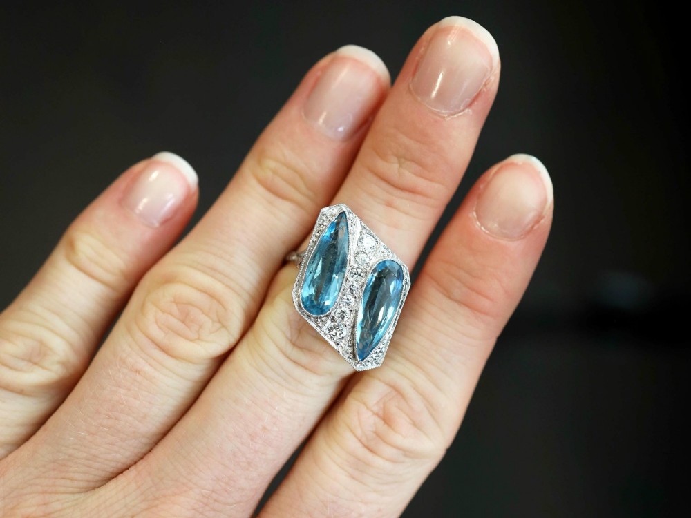 An Art Deco platinum cocktail ring featuring two pear-cut light blue aquamarines set diagonally beside a central row of round diamonds with millegrain borders. View III