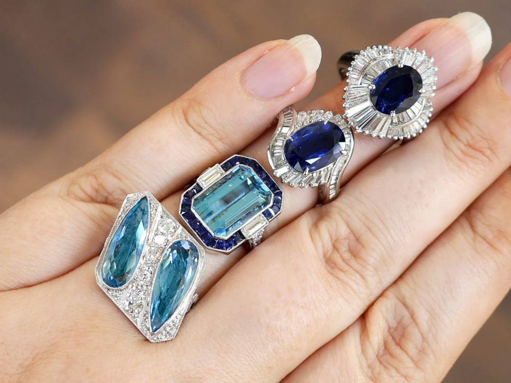 An Art Deco platinum cocktail ring featuring two pear-cut light blue aquamarines set diagonally beside a central row of round diamonds with millegrain borders. View IV