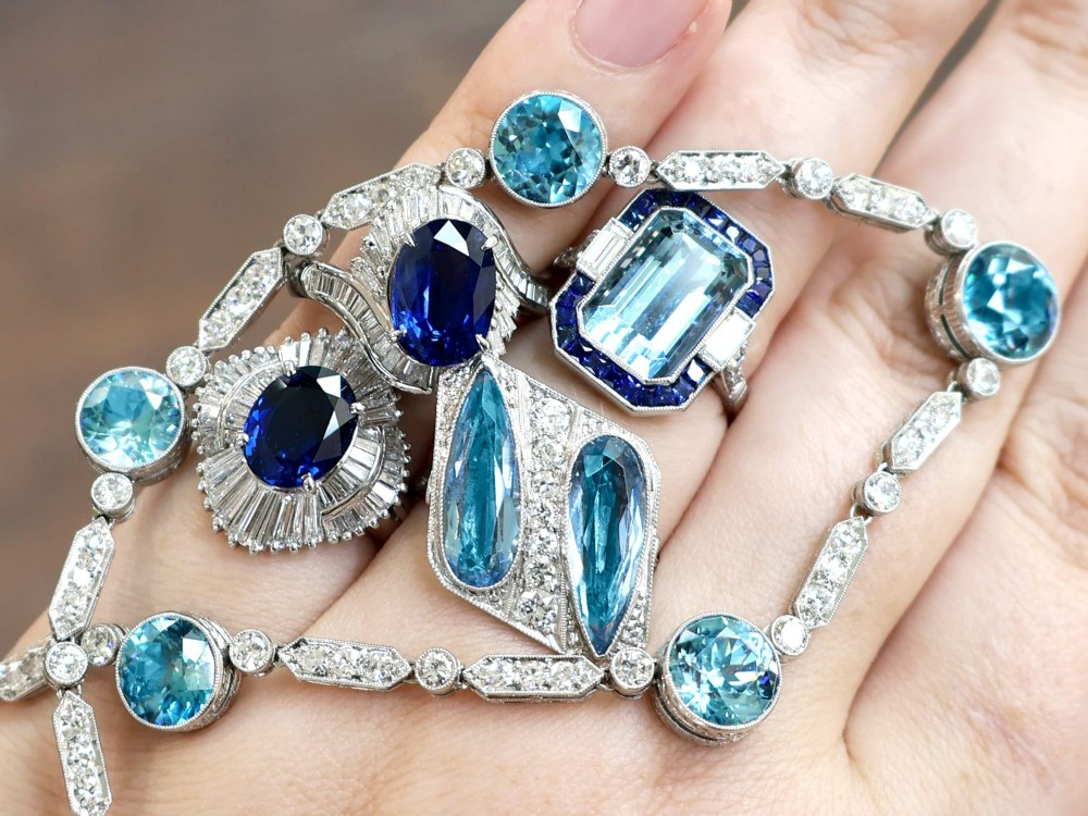 An Art Deco platinum cocktail ring featuring two pear-cut light blue aquamarines set diagonally beside a central row of round diamonds with millegrain borders. View V