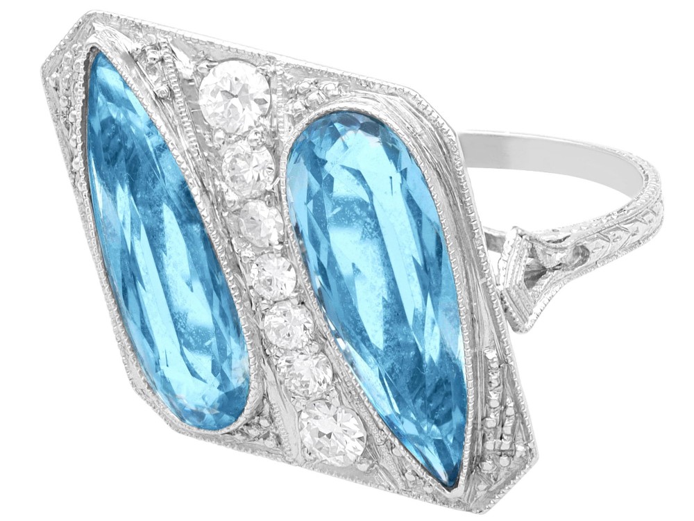An Art Deco platinum cocktail ring featuring two pear-cut light blue aquamarines set diagonally beside a central row of round diamonds with millegrain borders. View VI