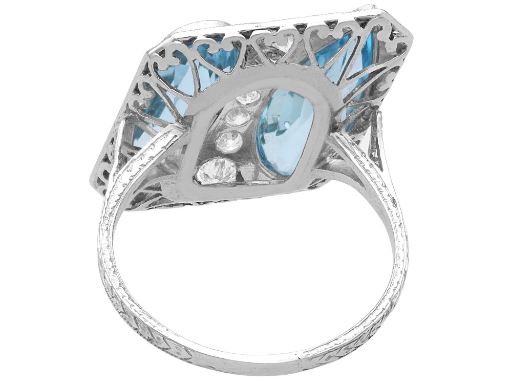 An Art Deco platinum cocktail ring featuring two pear-cut light blue aquamarines set diagonally beside a central row of round diamonds with millegrain borders. View VII
