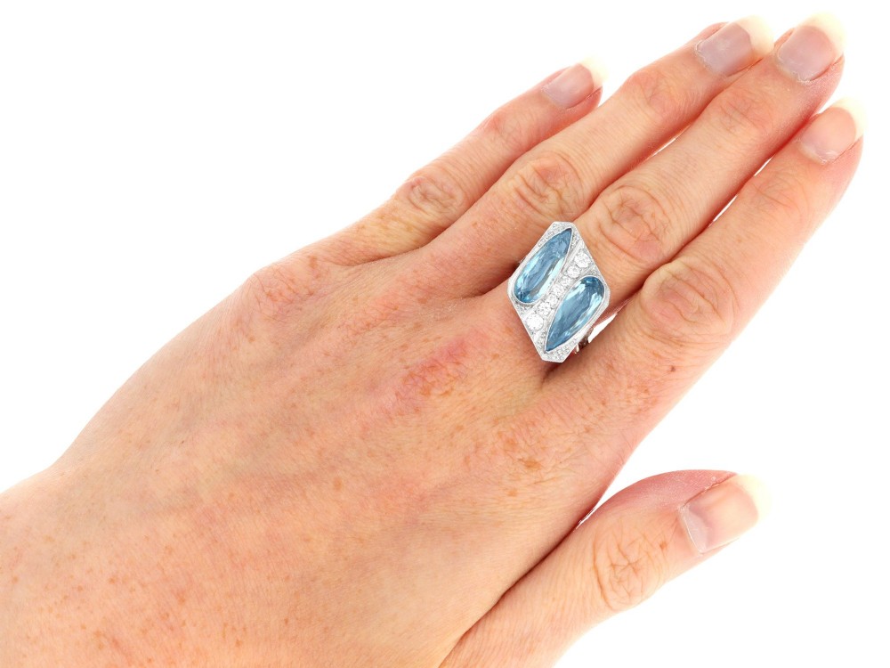 An Art Deco platinum cocktail ring featuring two pear-cut light blue aquamarines set diagonally beside a central row of round diamonds with millegrain borders. View X