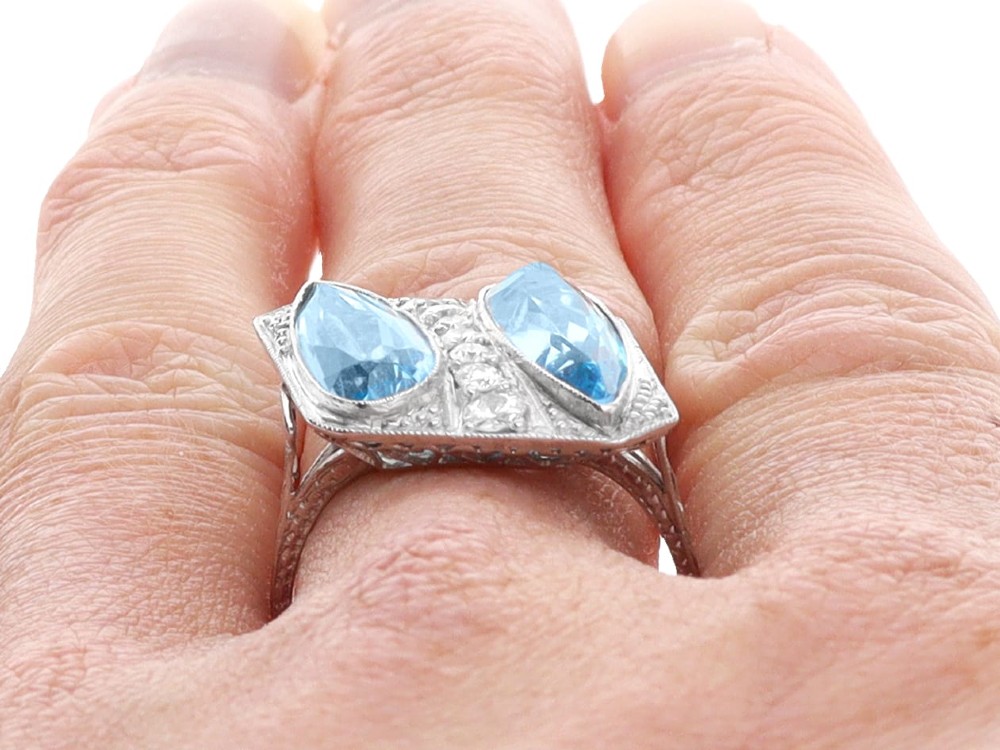 An Art Deco platinum cocktail ring featuring two pear-cut light blue aquamarines set diagonally beside a central row of round diamonds with millegrain borders. View XII