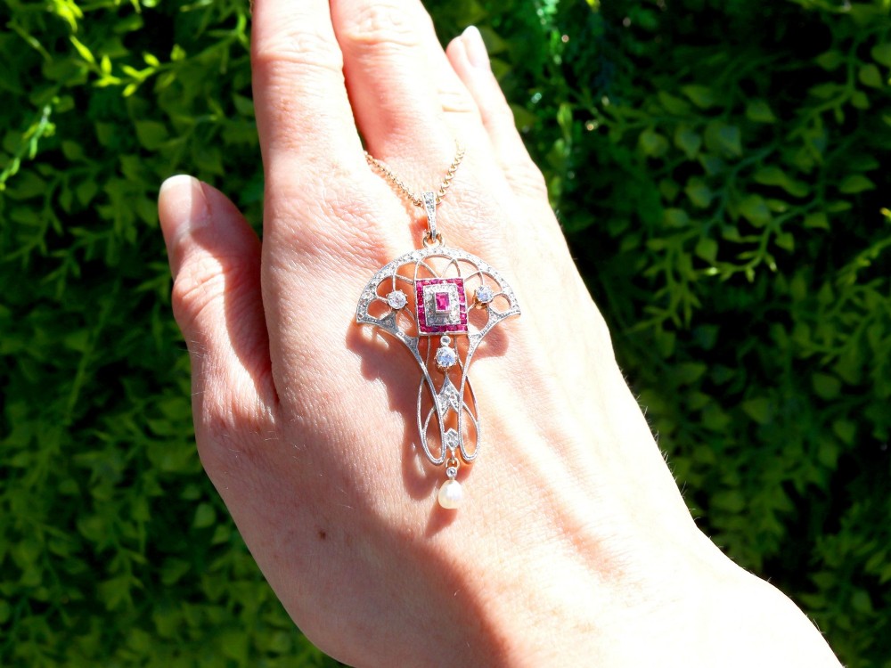 An Edwardian openwork yellow gold pendant set with a central square-cut ruby surrounded by small rubies, diamonds, and a suspended natural pearl drop. View II