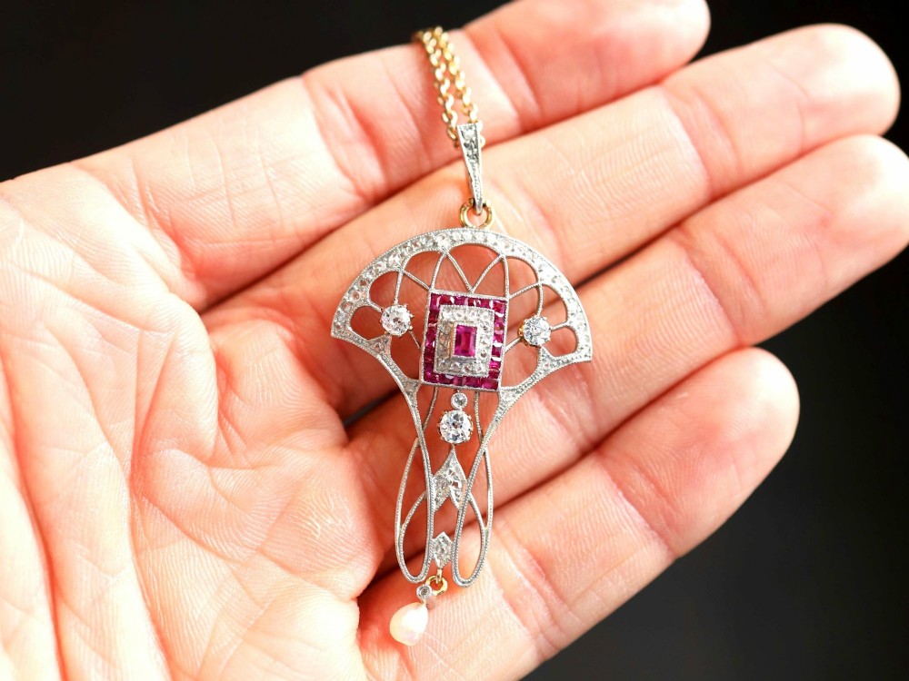 An Edwardian openwork yellow gold pendant set with a central square-cut ruby surrounded by small rubies, diamonds, and a suspended natural pearl drop. View III