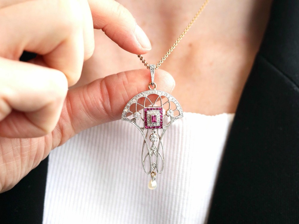 An Edwardian openwork yellow gold pendant set with a central square-cut ruby surrounded by small rubies, diamonds, and a suspended natural pearl drop. View V