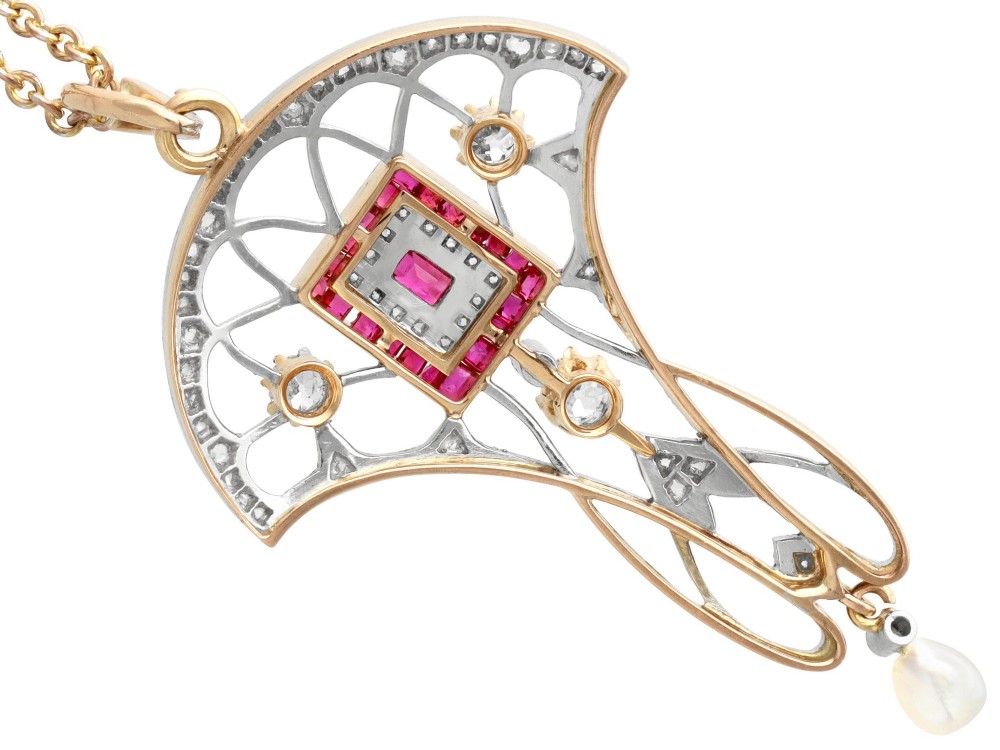 An Edwardian openwork yellow gold pendant set with a central square-cut ruby surrounded by small rubies, diamonds, and a suspended natural pearl drop. View X
