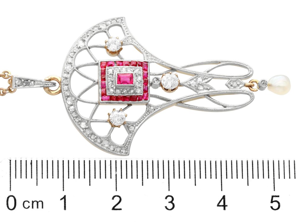 An Edwardian openwork yellow gold pendant set with a central square-cut ruby surrounded by small rubies, diamonds, and a suspended natural pearl drop. View XI