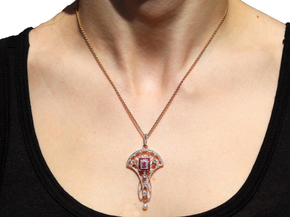An Edwardian openwork yellow gold pendant set with a central square-cut ruby surrounded by small rubies, diamonds, and a suspended natural pearl drop. View XIII