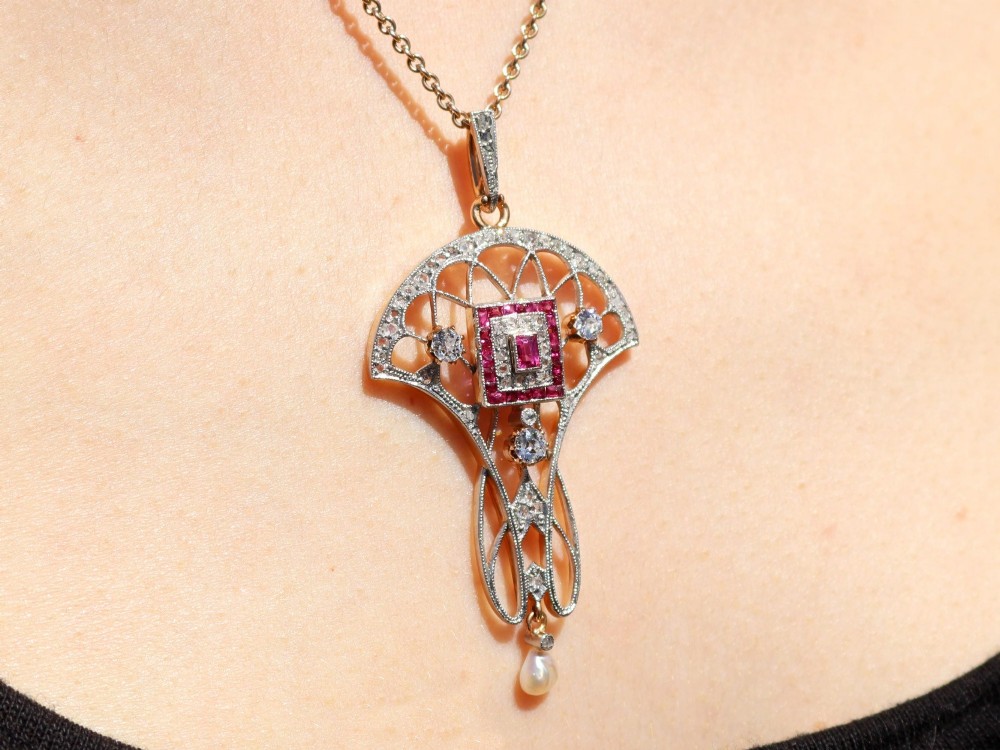 An Edwardian openwork yellow gold pendant set with a central square-cut ruby surrounded by small rubies, diamonds, and a suspended natural pearl drop. View XIV