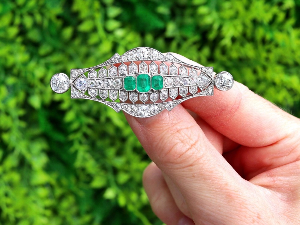 An Art Deco platinum brooch featuring three central step-cut green emeralds surrounded by a geometric lattice of diamonds with millegrain borders. View II