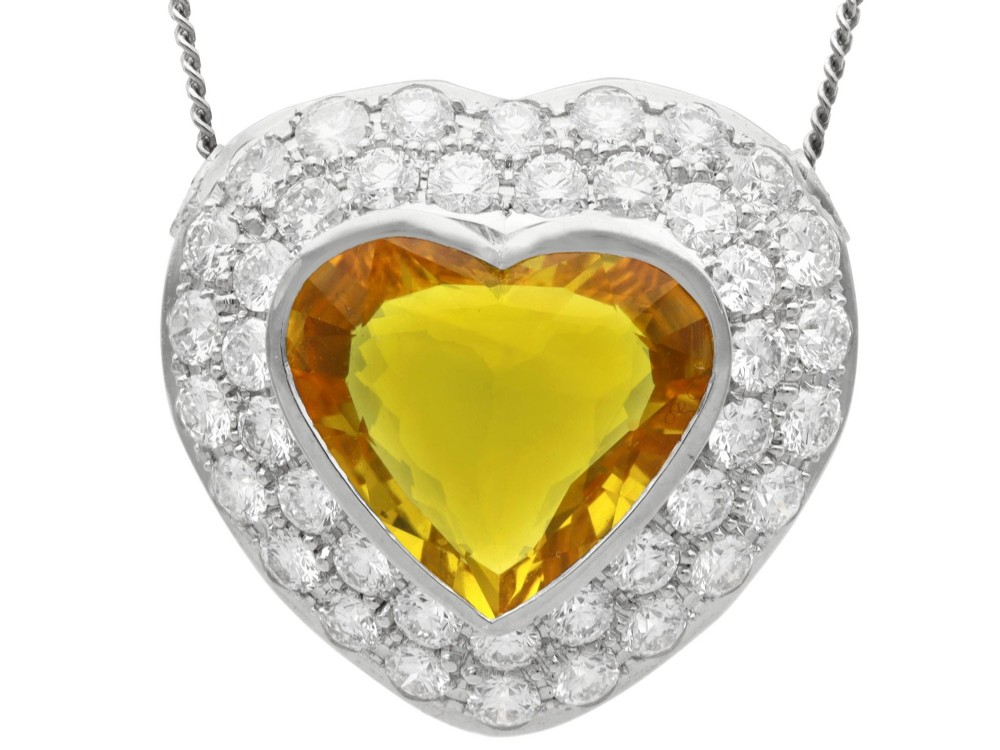 A platinum heart-shaped pendant set with a central faceted yellow sapphire surrounded by a double border of round diamonds.