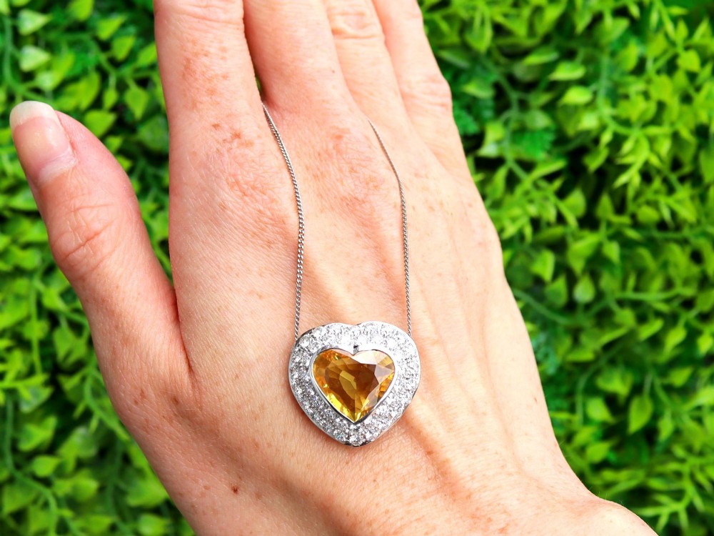 A platinum heart-shaped pendant set with a central faceted yellow sapphire surrounded by a double border of round diamonds. View II