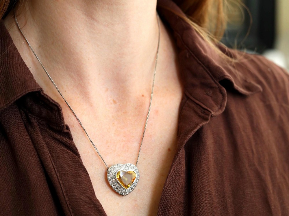 A platinum heart-shaped pendant set with a central faceted yellow sapphire surrounded by a double border of round diamonds. View III