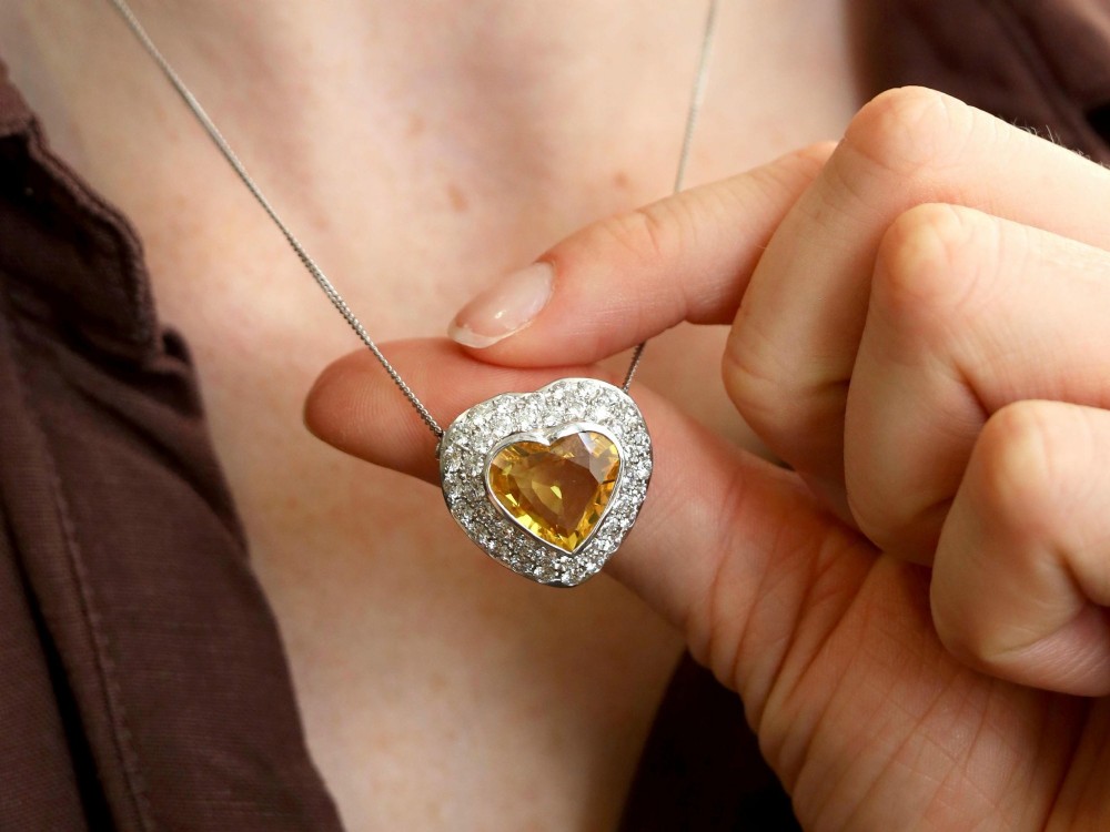 A platinum heart-shaped pendant set with a central faceted yellow sapphire surrounded by a double border of round diamonds. View IV