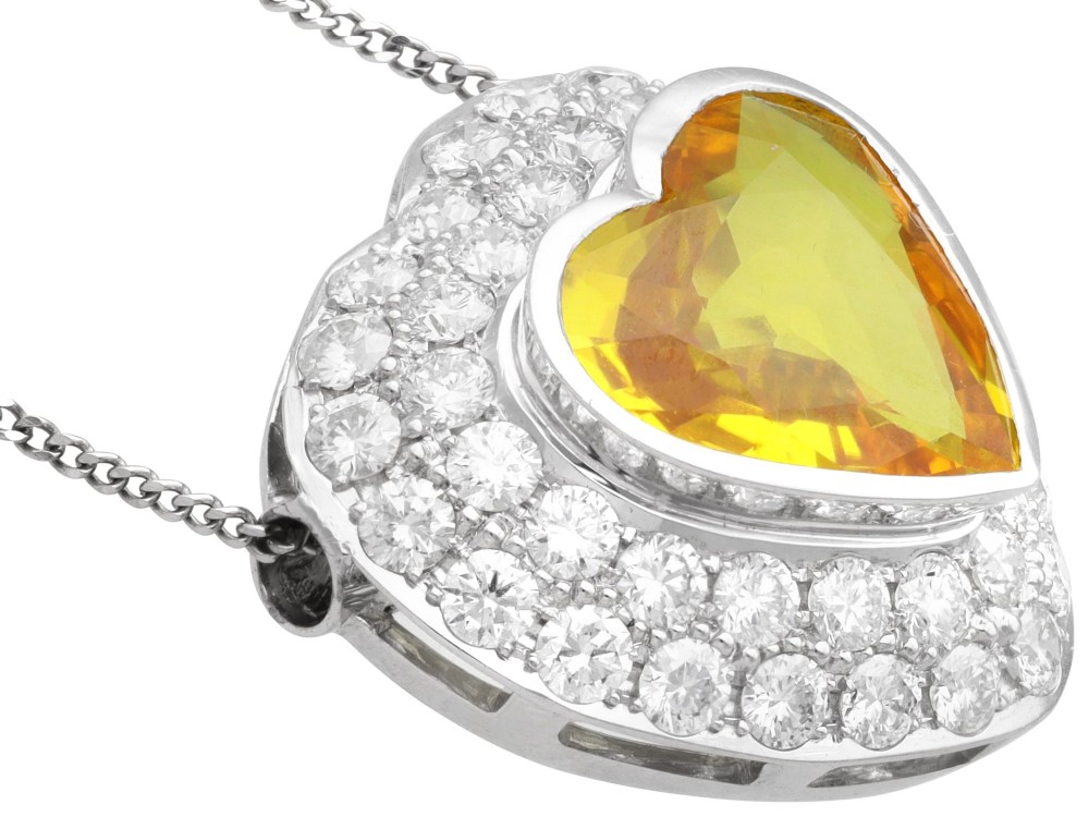 A platinum heart-shaped pendant set with a central faceted yellow sapphire surrounded by a double border of round diamonds. View X