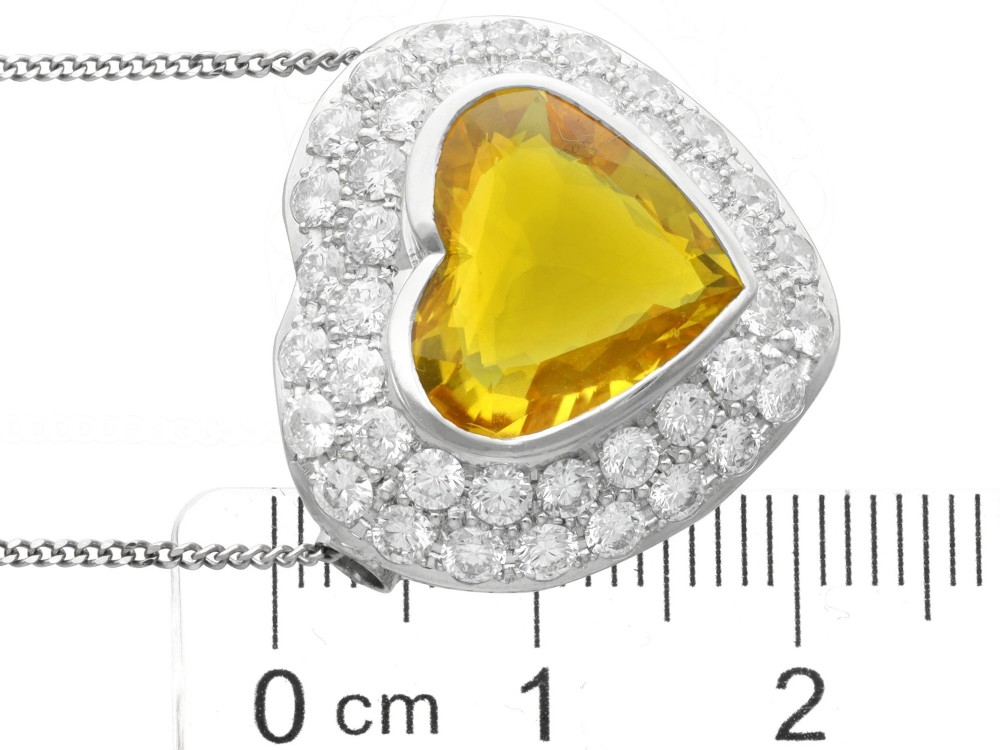 A platinum heart-shaped pendant set with a central faceted yellow sapphire surrounded by a double border of round diamonds. View XII
