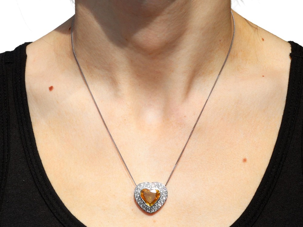 A platinum heart-shaped pendant set with a central faceted yellow sapphire surrounded by a double border of round diamonds. View XIV