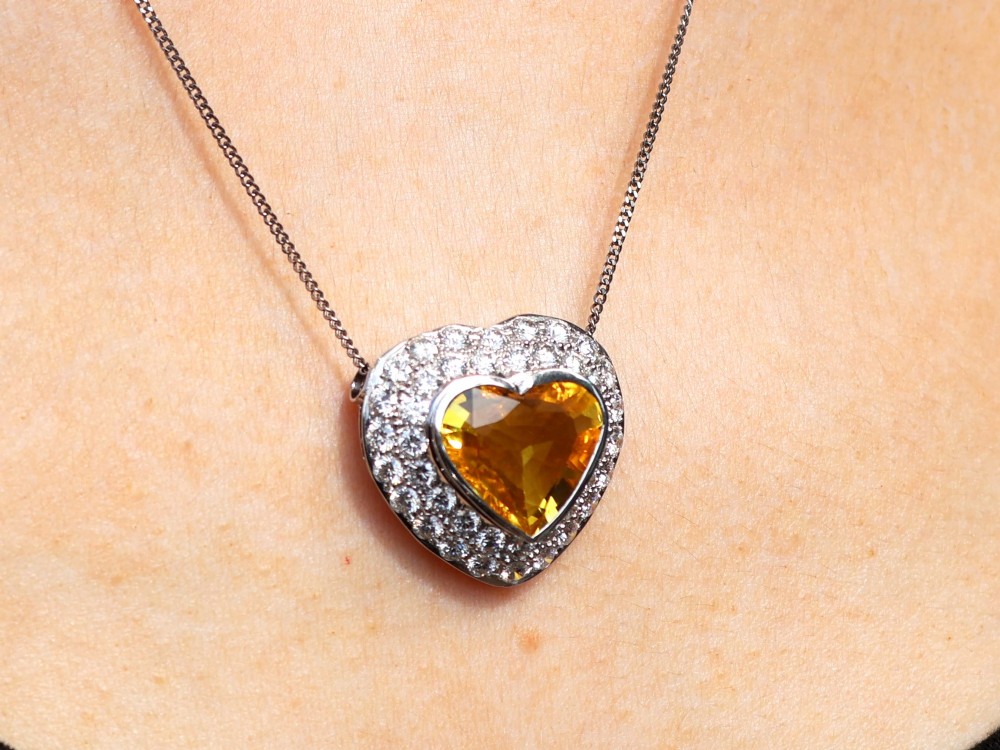 A platinum heart-shaped pendant set with a central faceted yellow sapphire surrounded by a double border of round diamonds. View XV