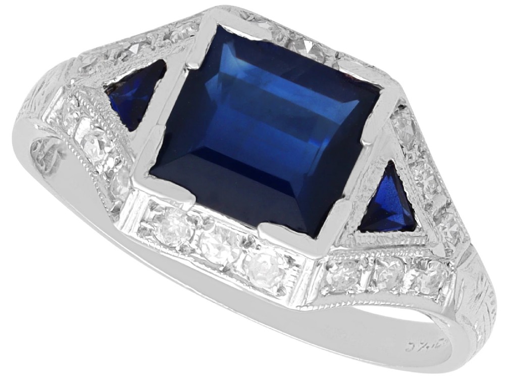 An Art Deco platinum ring featuring a central rectangular step-cut blue sapphire flanked by triangular sapphires and diamond-set shoulder details.