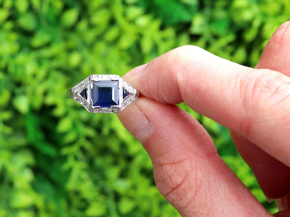 An Art Deco platinum ring featuring a central rectangular step-cut blue sapphire flanked by triangular sapphires and diamond-set shoulder details. View II