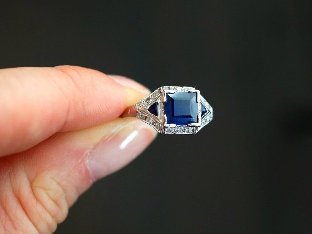 An Art Deco platinum ring featuring a central rectangular step-cut blue sapphire flanked by triangular sapphires and diamond-set shoulder details. View III