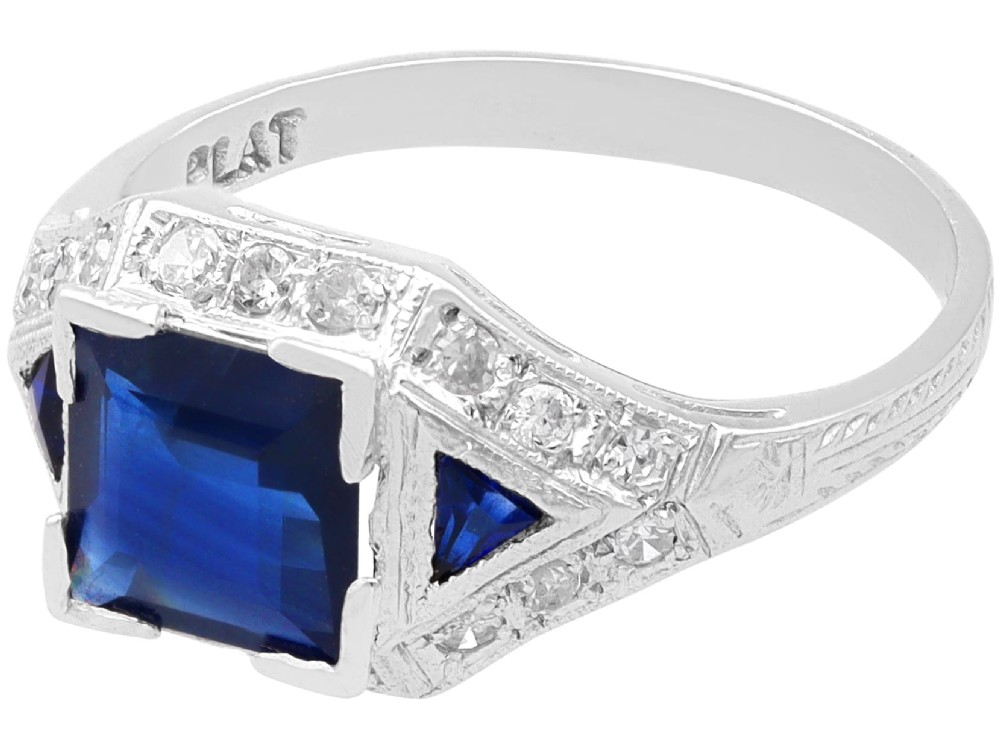 An Art Deco platinum ring featuring a central rectangular step-cut blue sapphire flanked by triangular sapphires and diamond-set shoulder details. View V