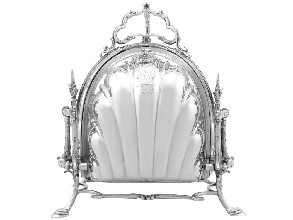 An antique Victorian sterling silver folding biscuit box featuring shell-form compartments, an ornate looped handle, and an engraved 1897 monogram.