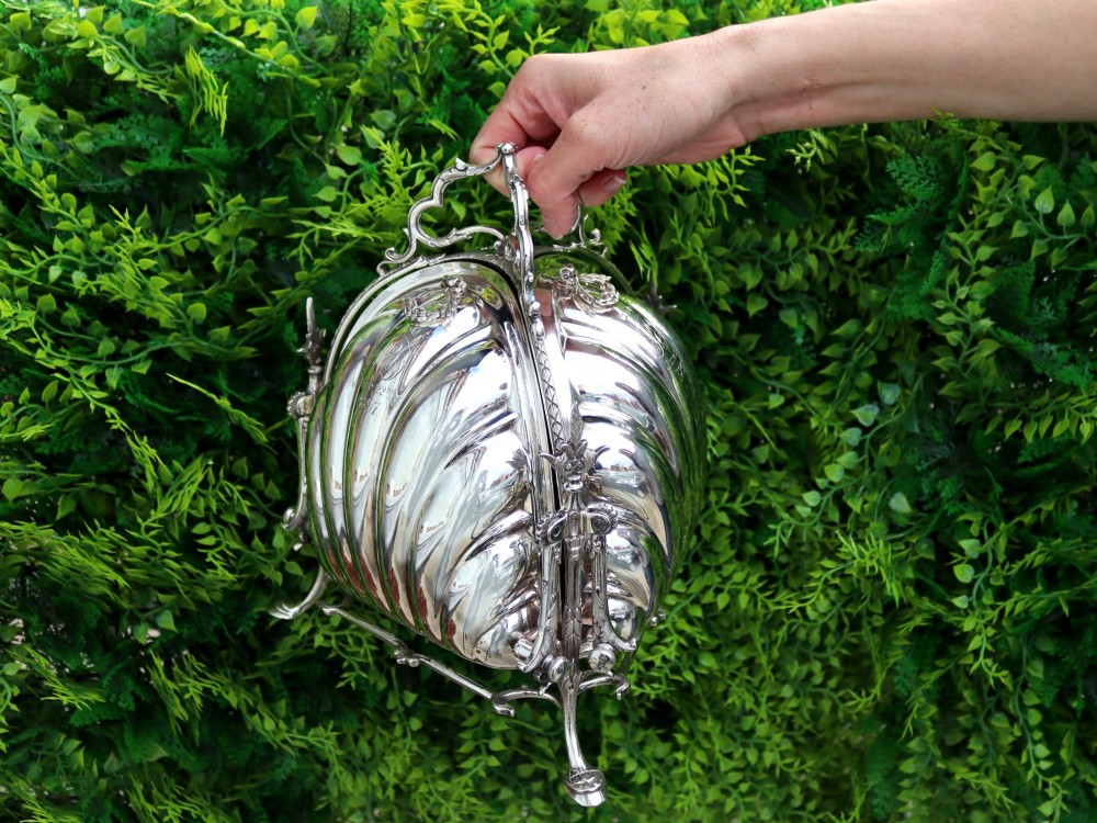 An antique Victorian sterling silver folding biscuit box featuring shell-form compartments, an ornate looped handle, and an engraved 1897 monogram. View III