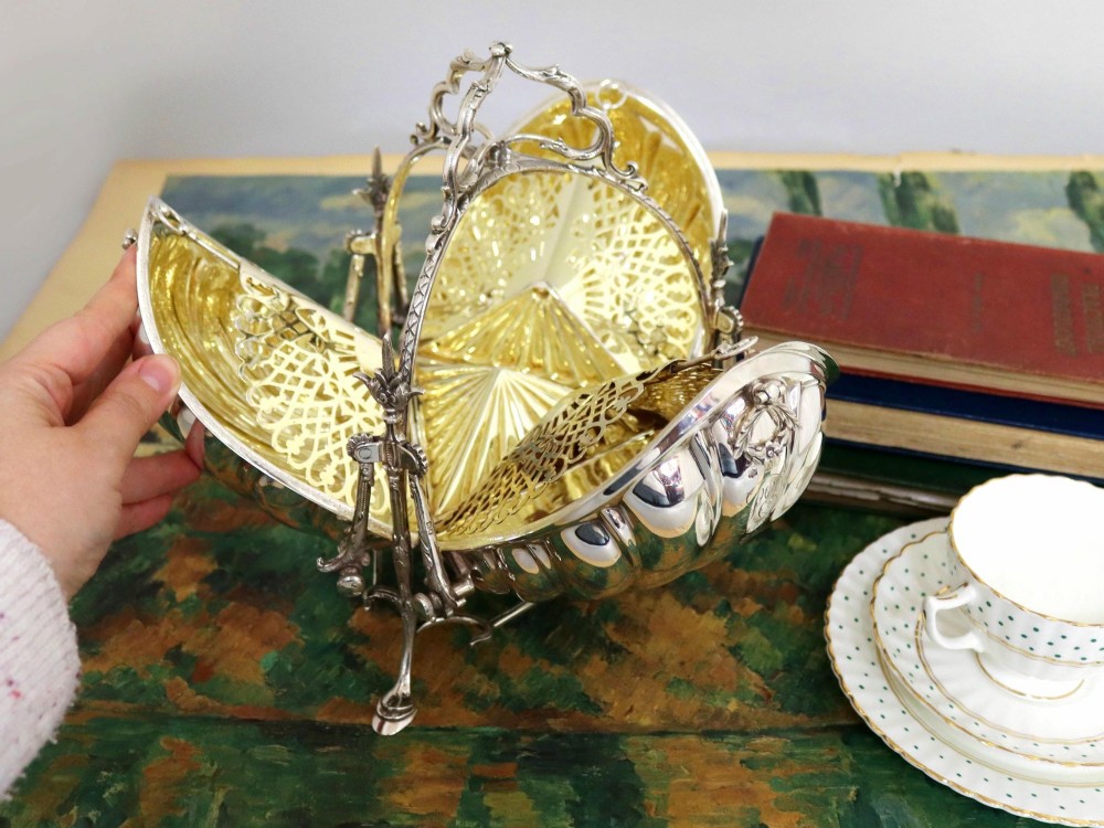 An antique Victorian sterling silver folding biscuit box featuring shell-form compartments, an ornate looped handle, and an engraved 1897 monogram. View IV