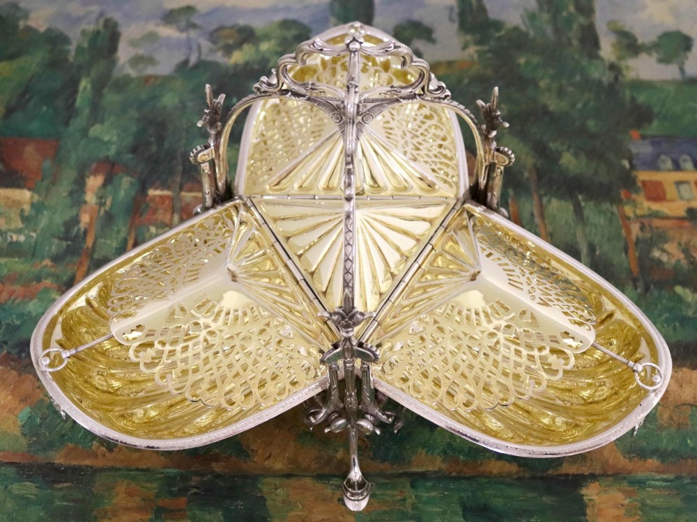 An antique Victorian sterling silver folding biscuit box featuring shell-form compartments, an ornate looped handle, and an engraved 1897 monogram. View V
