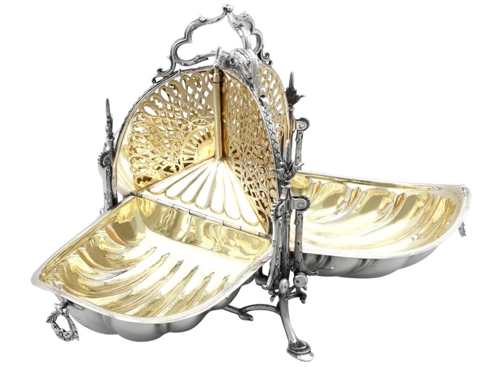 An antique Victorian sterling silver folding biscuit box featuring shell-form compartments, an ornate looped handle, and an engraved 1897 monogram. View VIII