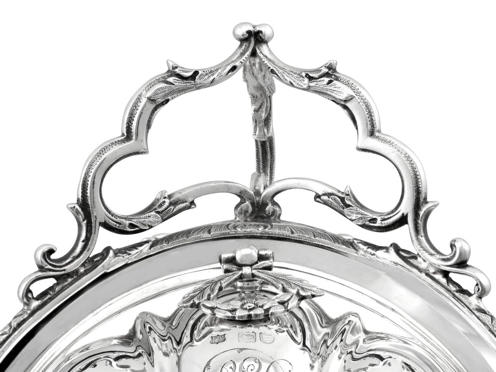 An antique Victorian sterling silver folding biscuit box featuring shell-form compartments, an ornate looped handle, and an engraved 1897 monogram. View IX