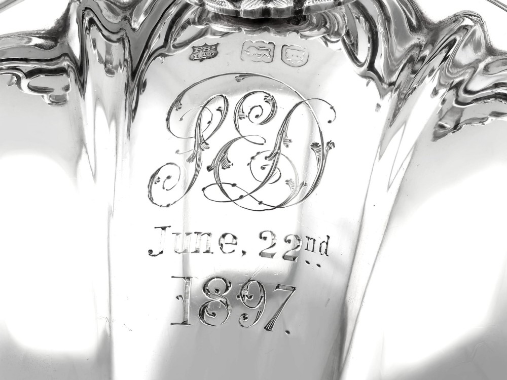An antique Victorian sterling silver folding biscuit box featuring shell-form compartments, an ornate looped handle, and an engraved 1897 monogram. View XII