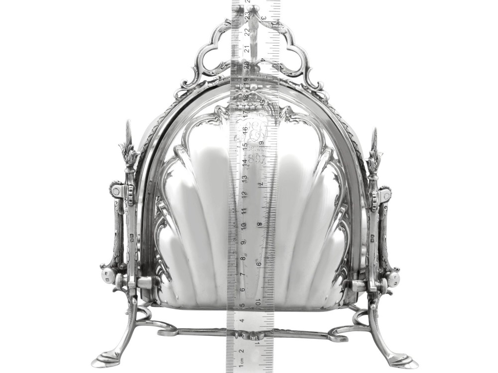 An antique Victorian sterling silver folding biscuit box featuring shell-form compartments, an ornate looped handle, and an engraved 1897 monogram. View XV