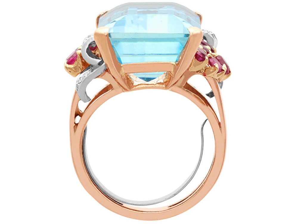 A 1940s Retro rose gold cocktail ring set with a large emerald-cut aquamarine flanked by ruby clusters and diamond accents. View VIII